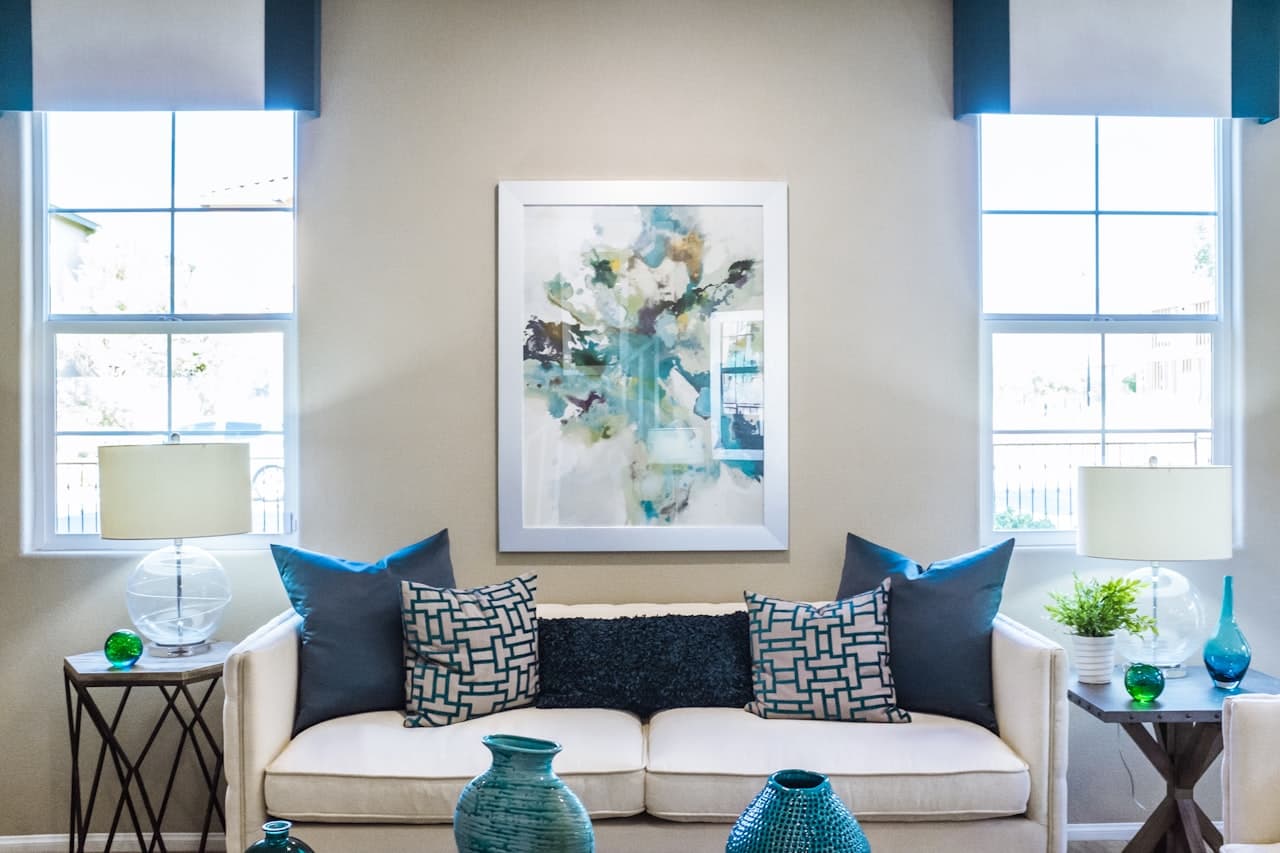 A stylish staged living room with a white couch, teal accent pillows, and framed abstract art